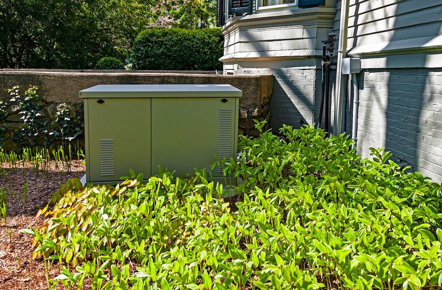 Generator on the side of a house with bushes surrounding it